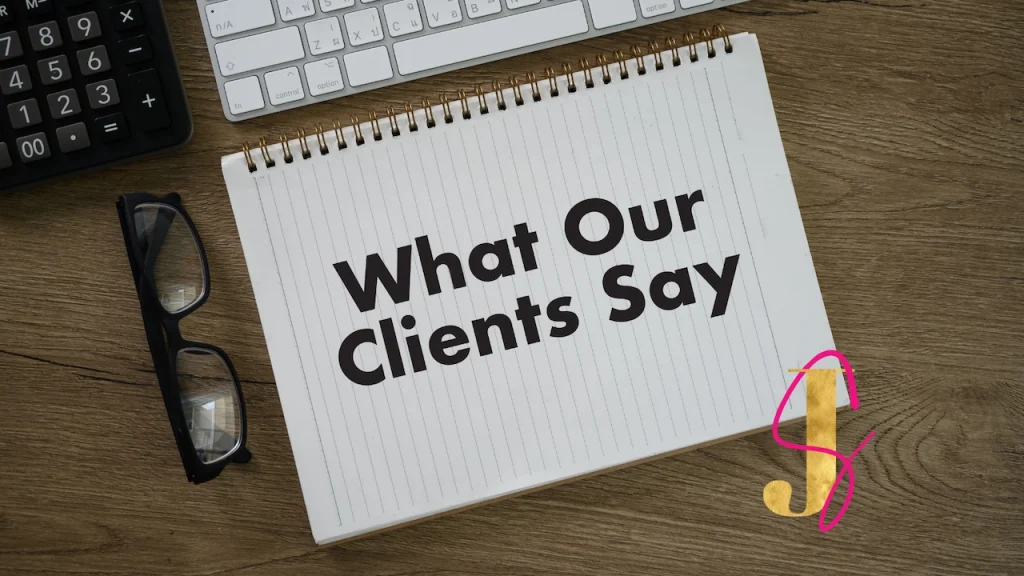 An open notebook on a wooden table with the words What Our Clients Say. Glasses and a keyboard also sit on the desk
