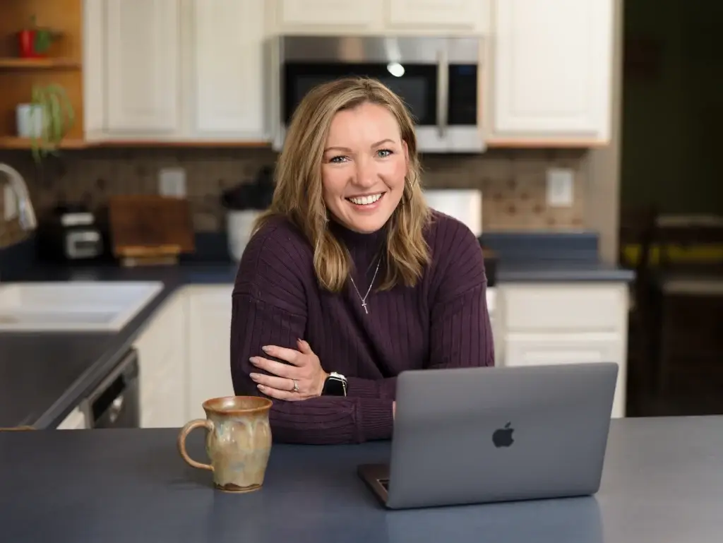 Jennifer Sakowski smiling at her kitchen island with a laptop and coffee mug