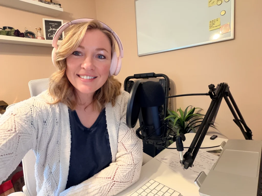 Raney Day Design founder and business strategist, Jennifer Sakowski, sits at her desk with a microphone and laptop computer while wearing headphones