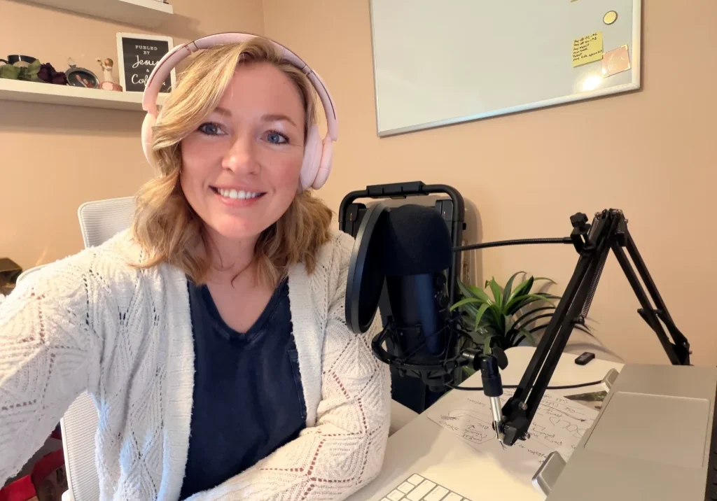 Raney Day Design founder and business strategist, Jennifer Sakowski, sits at her desk with a microphone and laptop computer while wearing headphones
